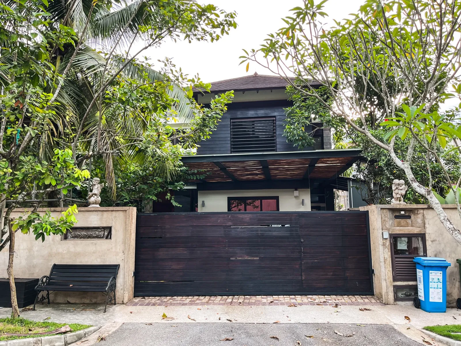 A two-storey landed house in Fuyong Estate, Bukit Panjang, with a dark timber gate and mature trees overhanging the boundary wall
