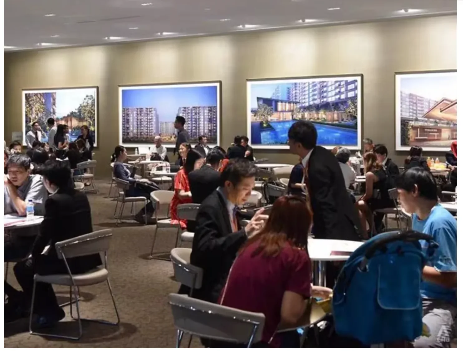 Home buyers at a Singapore condominium sales gallery, seated at tables with agents in front of large project renders