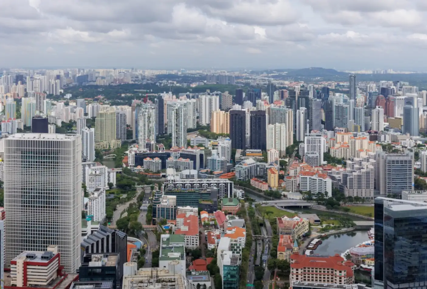 Singapore's skyline seen from CapitaSpring, with office towers and low-rise conserved buildings along a river in the foreground and residential towers stretching to the horizon