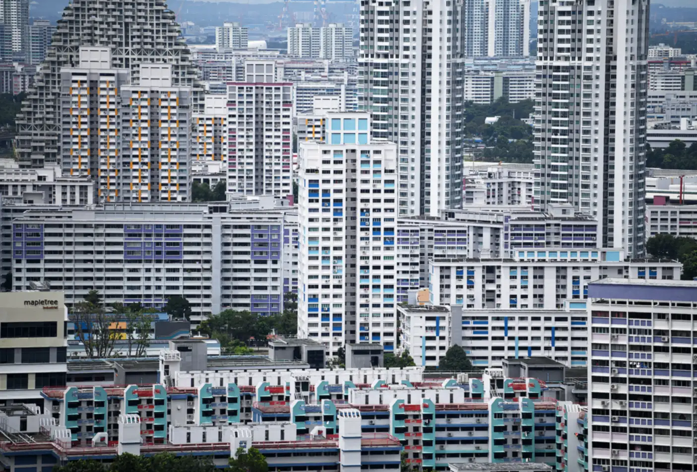 Rows of HDB blocks of different ages and heights packed together, from low older blocks with teal and red trim in front to tall white towers with blue and purple accents behind, under a hazy sky