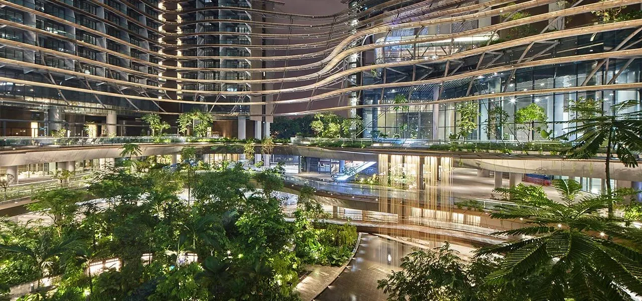 The Green Heart of Marina One at night — layered gardens and curved balconies rising around the development's central biodiversity garden