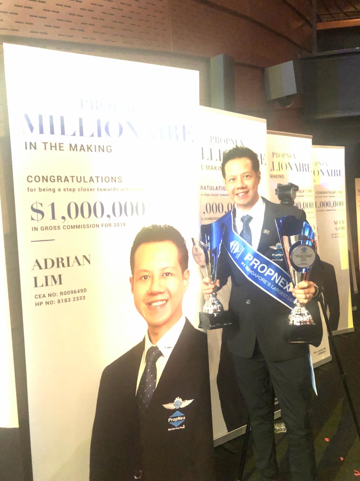 Adrian holding two trophies in front of the Millionaire-in-the-Making banner with his name and $1,000,000 in Gross Commission for 2018