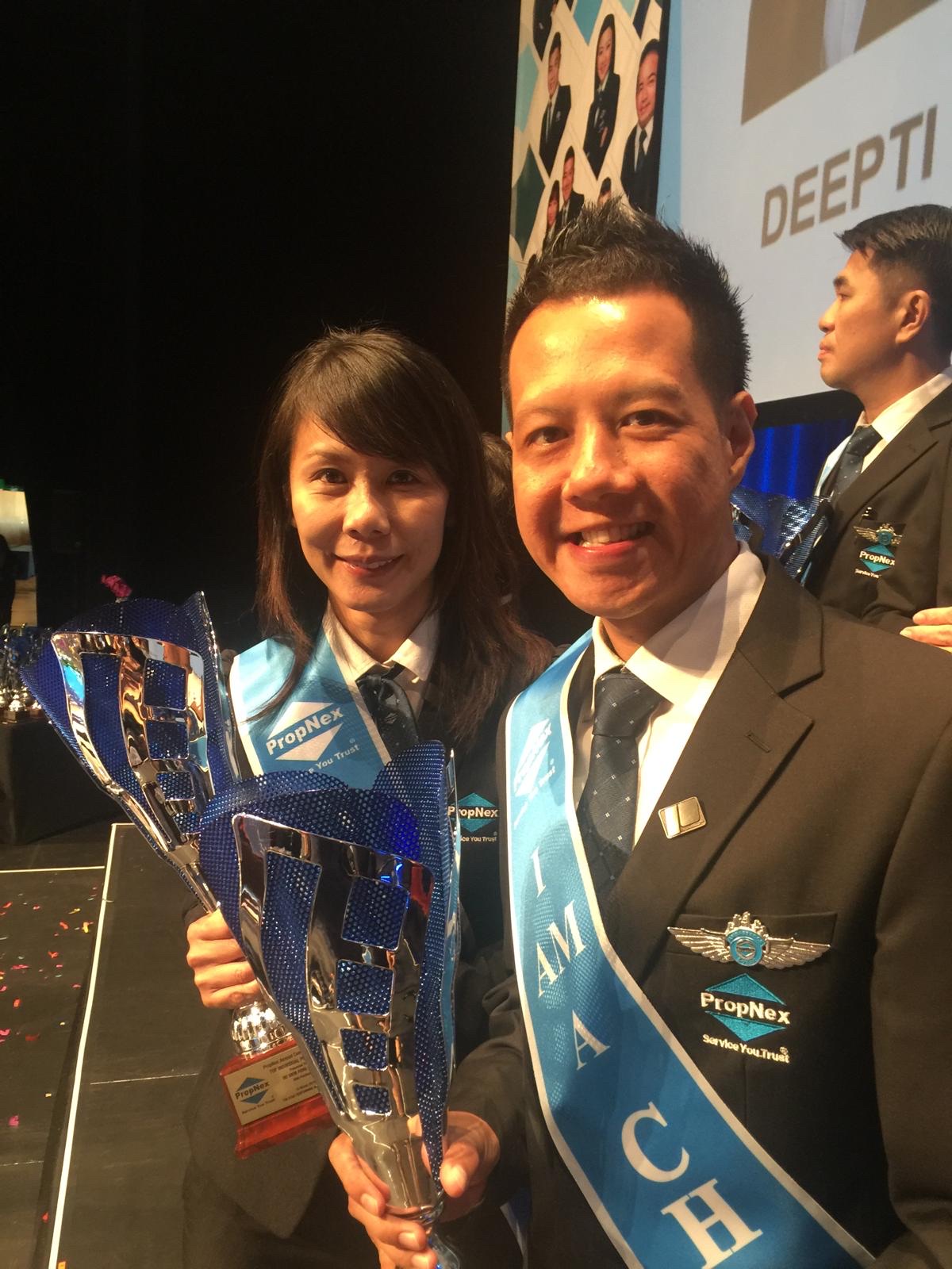 Adrian wearing the PropNex Champion sash with a female colleague holding a large blue trophy