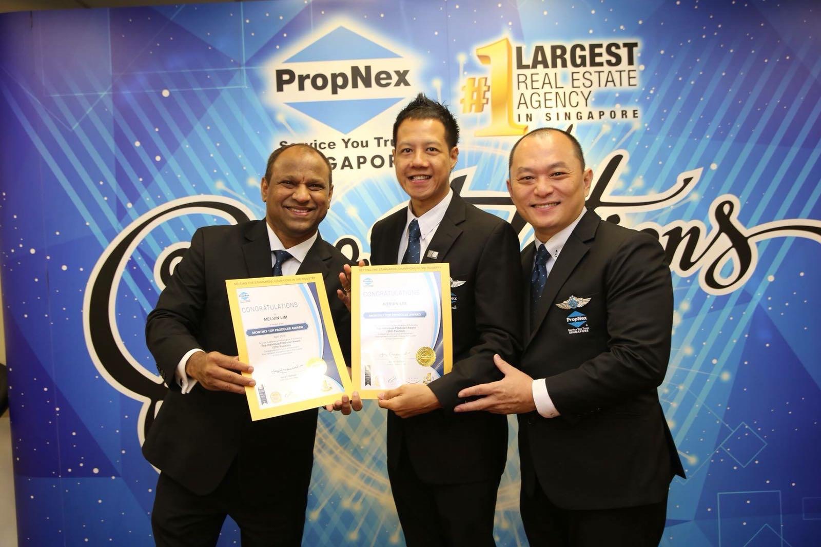 Adrian standing centre with two colleagues holding congratulations certificates in front of the PropNex #1 Largest Real Estate Agency backdrop