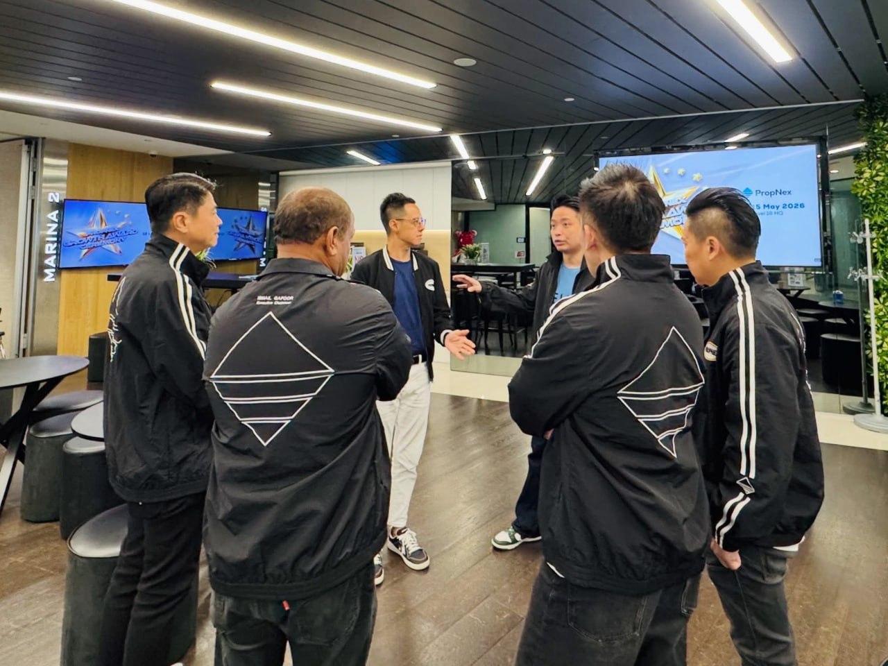 Adrian in conversation with a small group of agents in PropNex Power Movers jackets at PropNex HQ