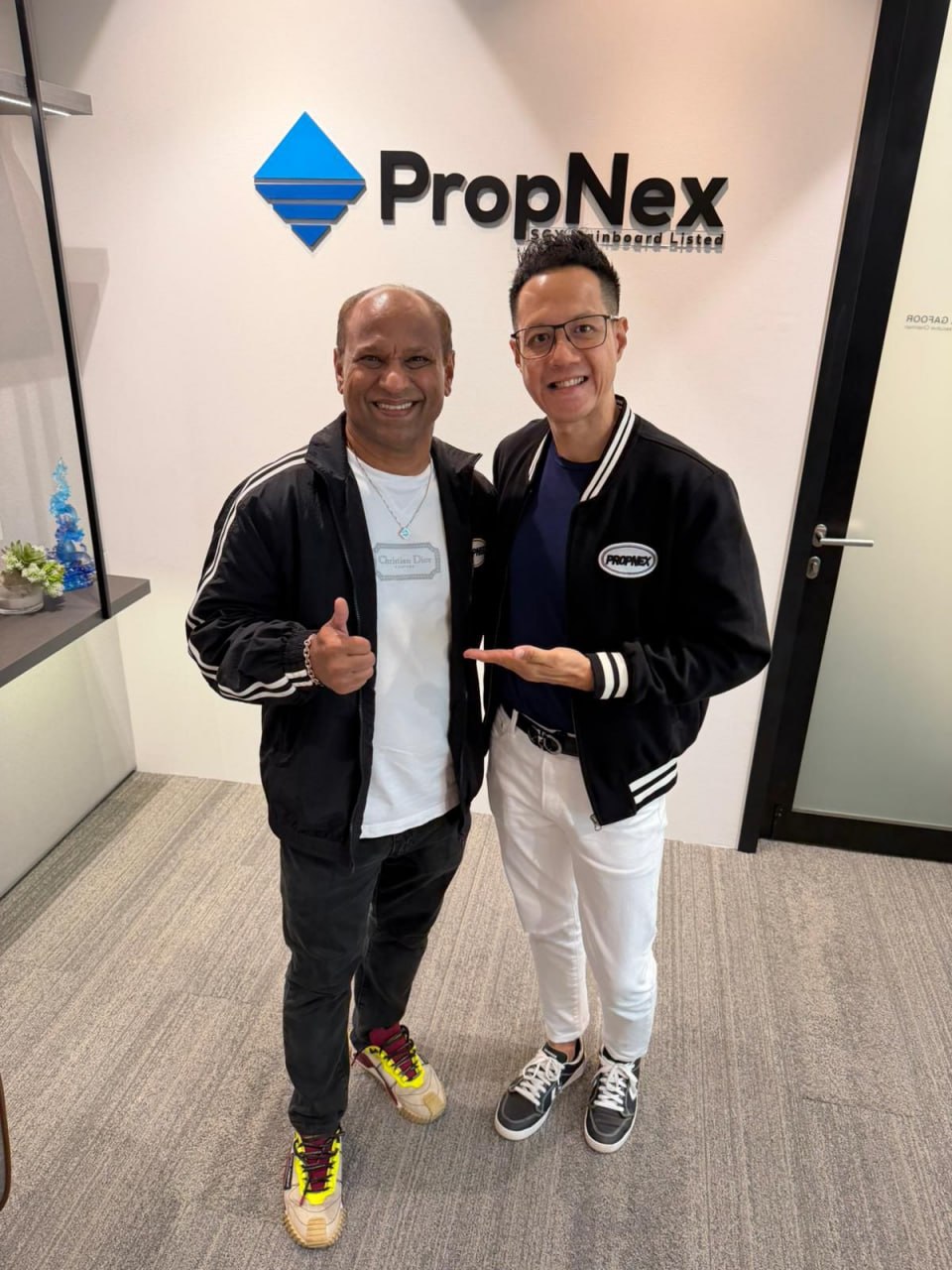 Adrian and PropNex co-founder Ismail Gafoor posing together in front of the PropNex SGX Mainboard Listed wall